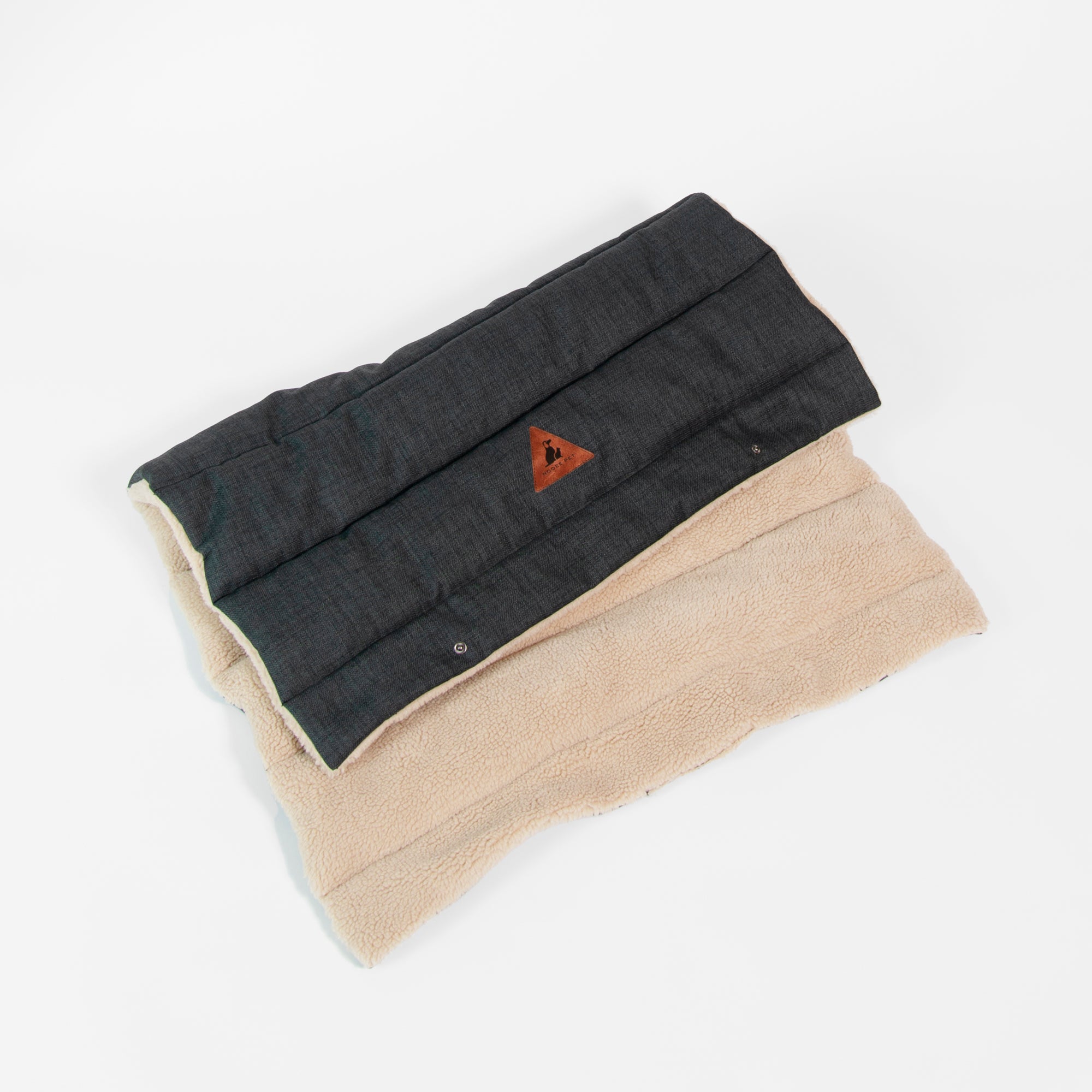 Folded Nooee Pet Jack Mat showing both sides—dark charcoal quilted fabric and soft beige sherpa lining—with stitched logo patch visible.