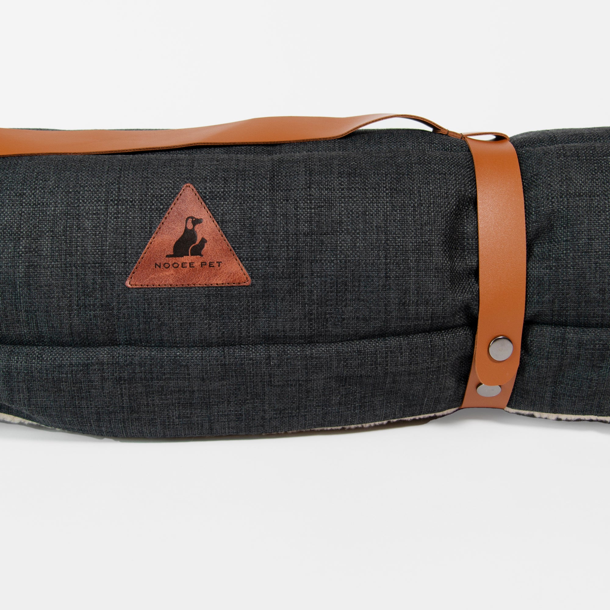 Close-up of the rolled Nooee Pet Jack Mat in black with brown vegan leather straps and a triangular Nooee Pet logo patch.