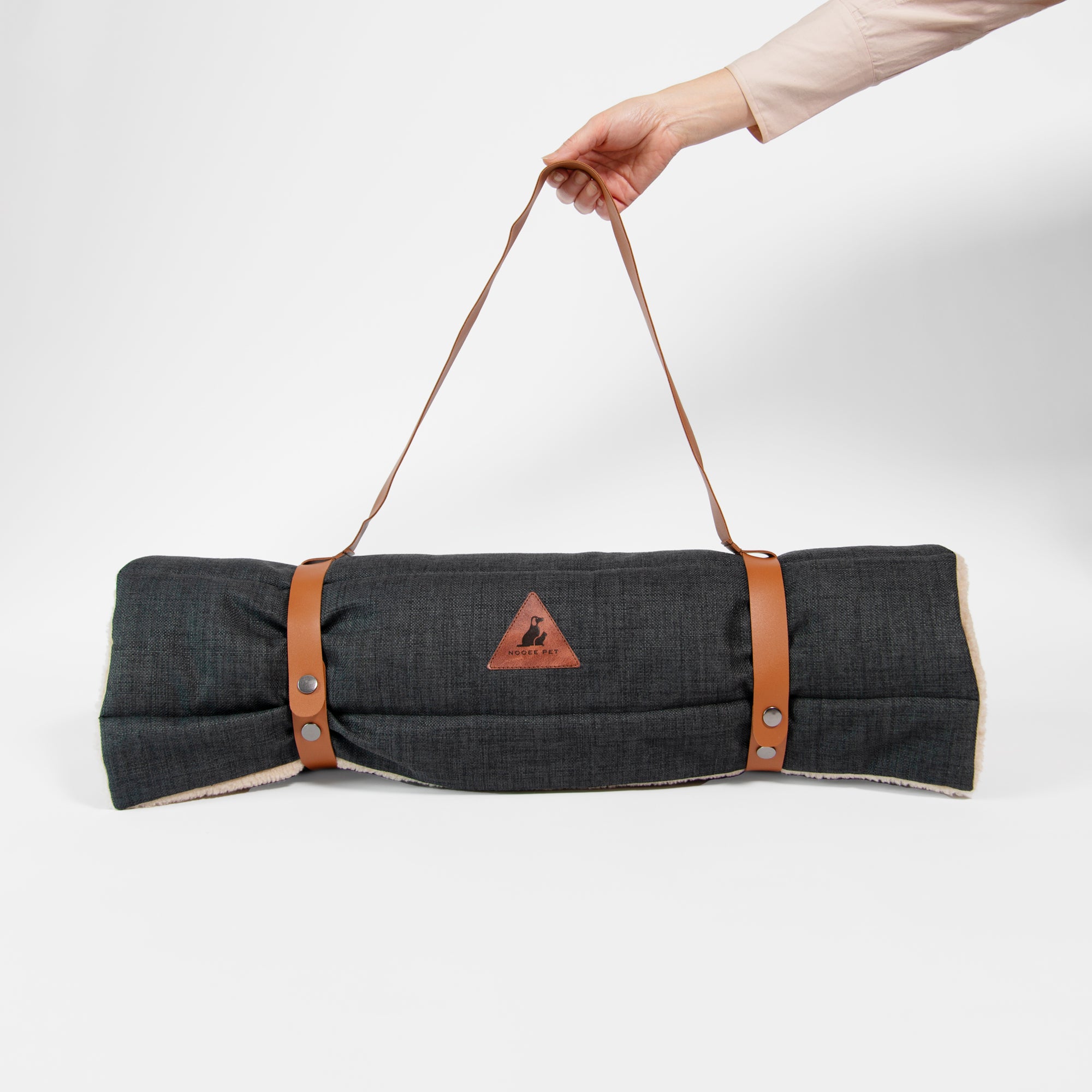 Rolled-up Nooee Pet Jack Mat in black fabric with brown vegan leather handle, held by hand for easy carrying.