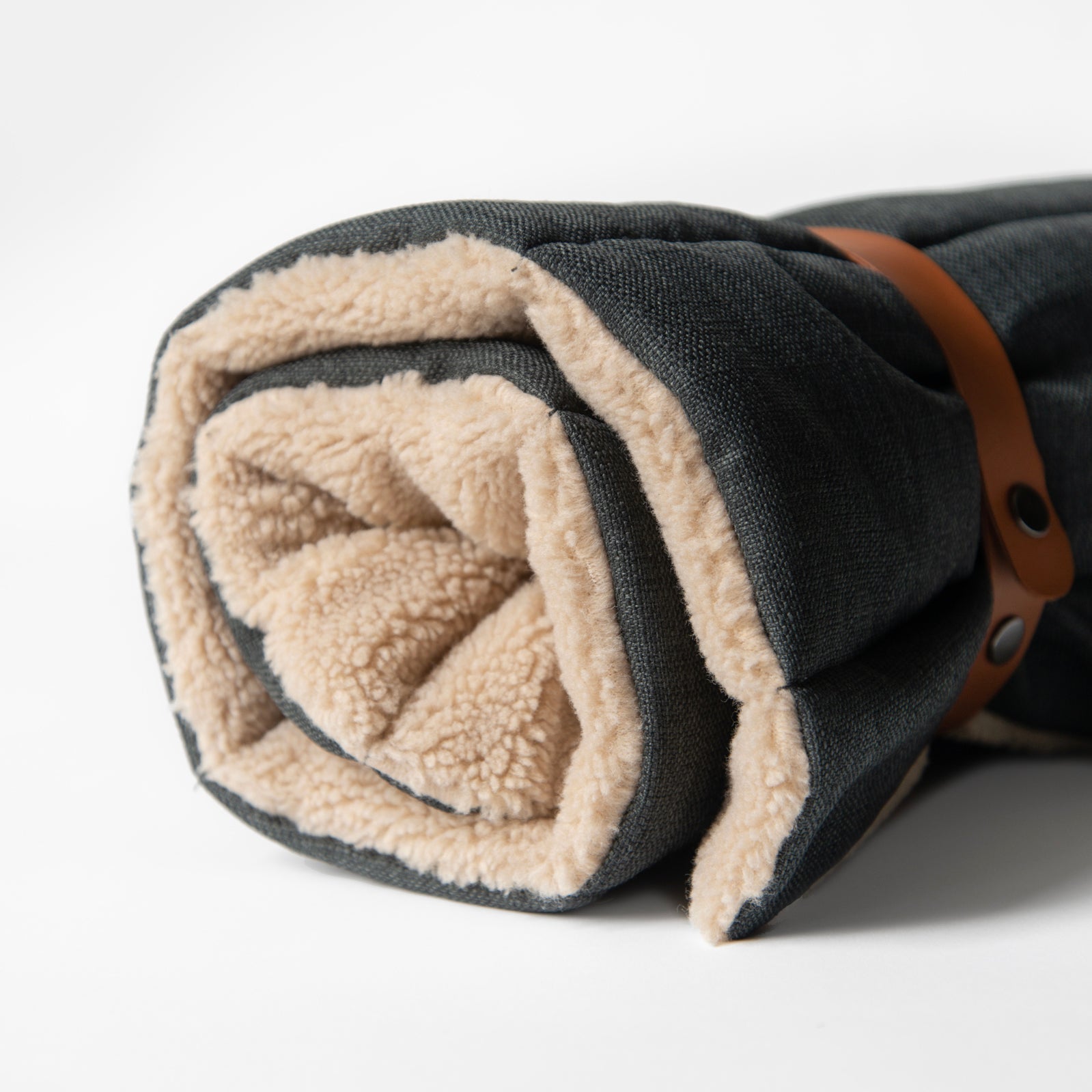 Rolled-up Nooee Pet Jack Mat showing soft beige sherpa interior and black exterior, secured with brown vegan leather straps.