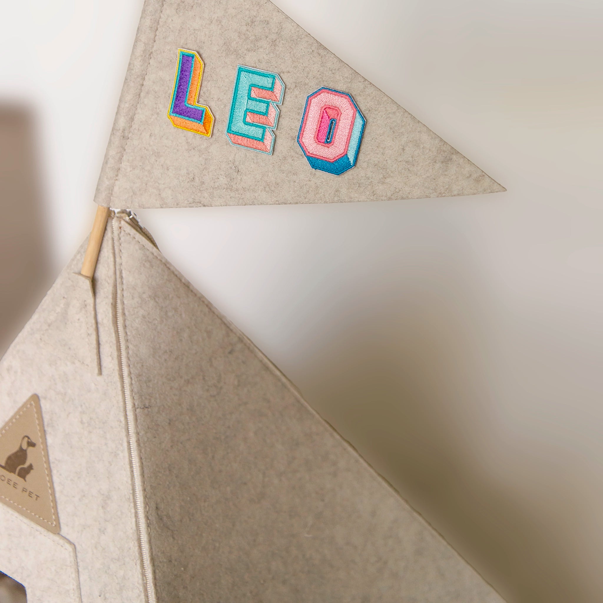 Close-up of a teepee flag with colorful embroidered letters spelling “LEO,” mounted on top of a Nooee Pet teepee in matching felt material.