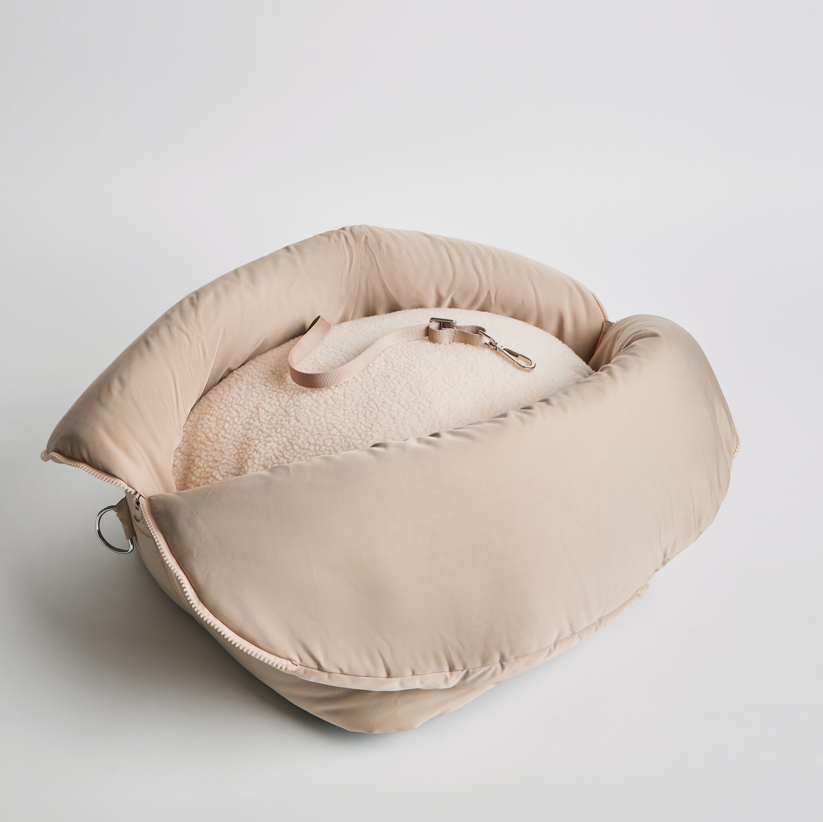 Top view of the Nooee Pet Lola Car Seat in cream nylon, showcasing its soft padded structure and inner safety tether on a removable fleece cushion.