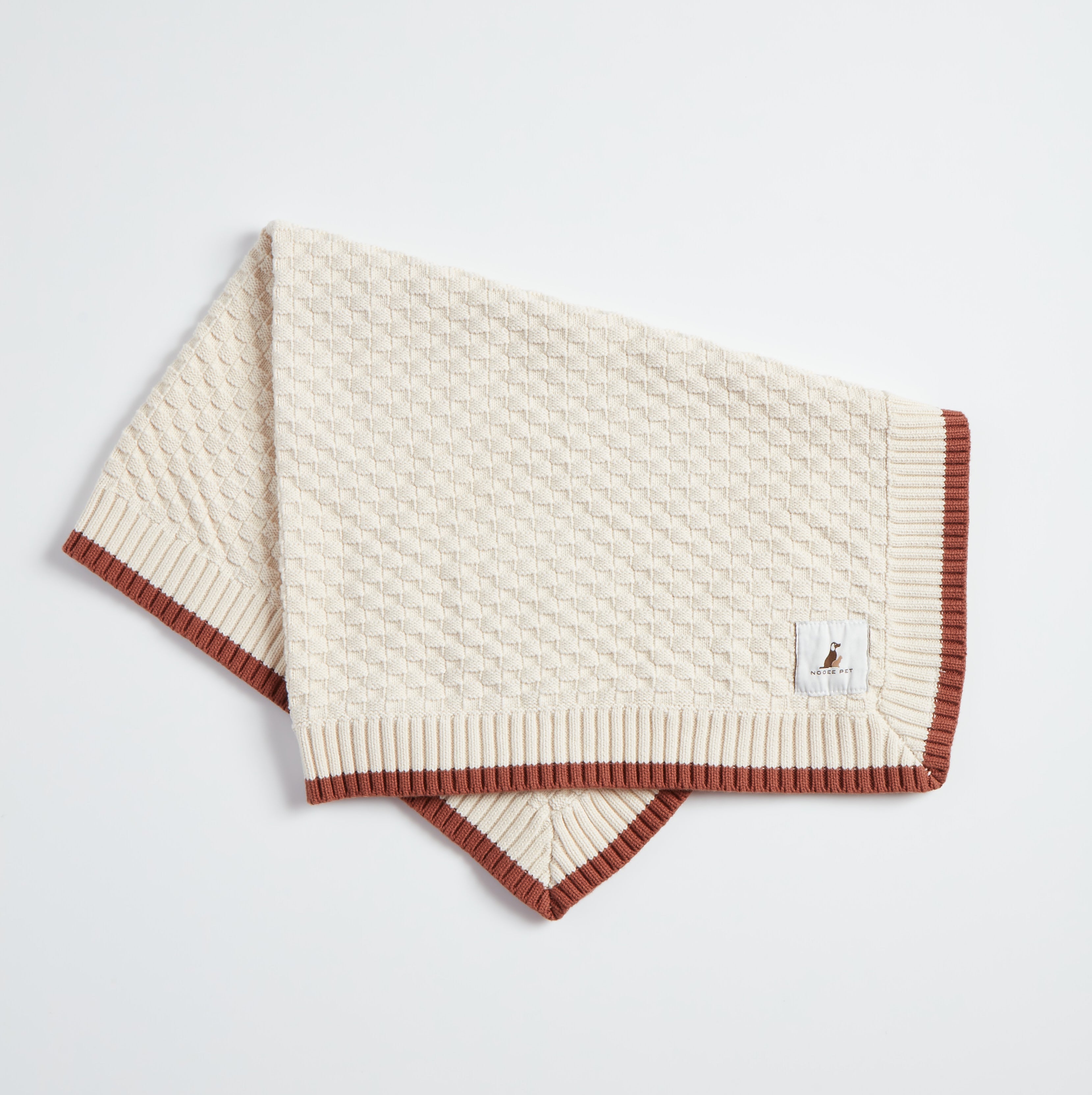 Folded Nooee Pet Organic Cotton Blanket in cream with brown ribbed trim, displayed flat on a white background.