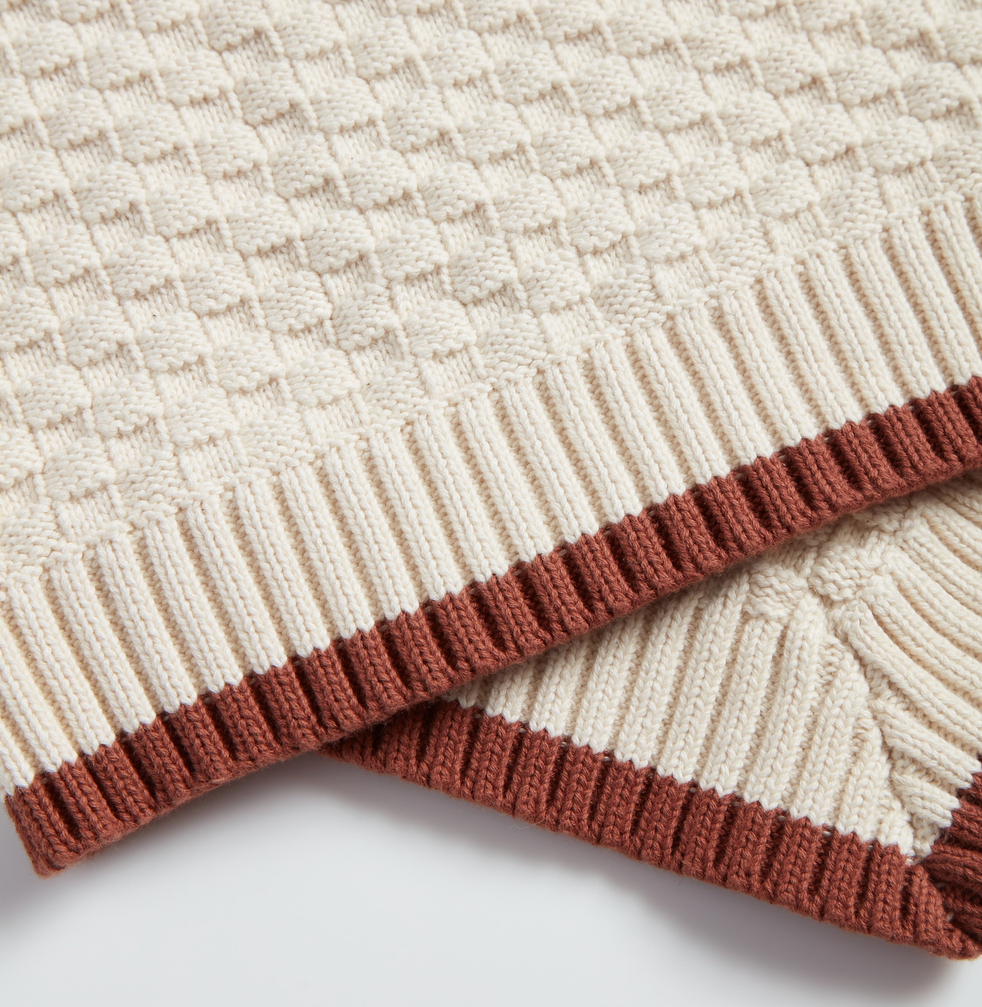 Close-up of Nooee Pet Organic Cotton Blanket showcasing the textured knit pattern and ribbed brown trim on cream-colored fabric.
