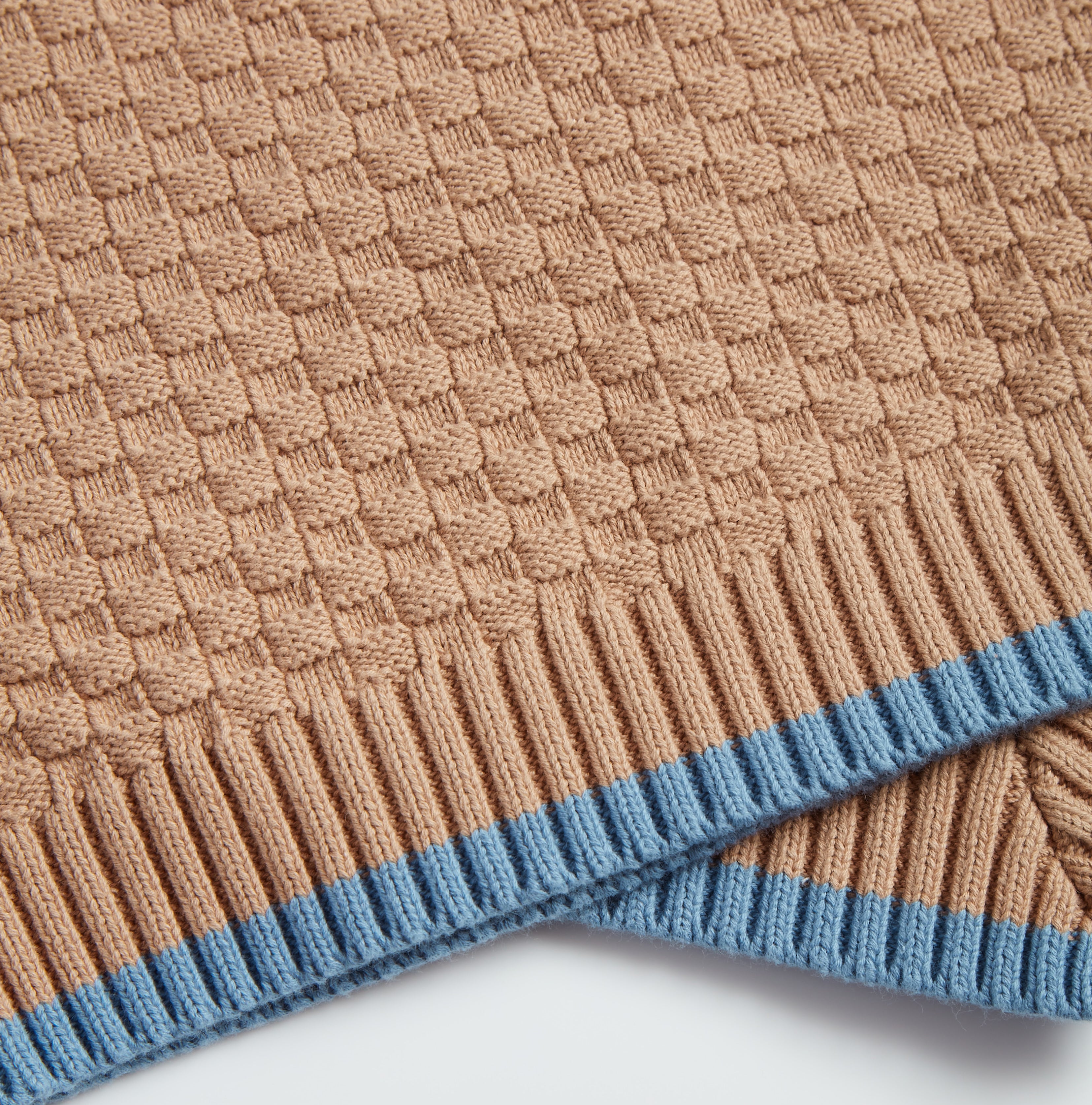Close-up of brown Nooee Pet organic cotton blanket featuring a waffle-knit pattern and light blue ribbed trim.