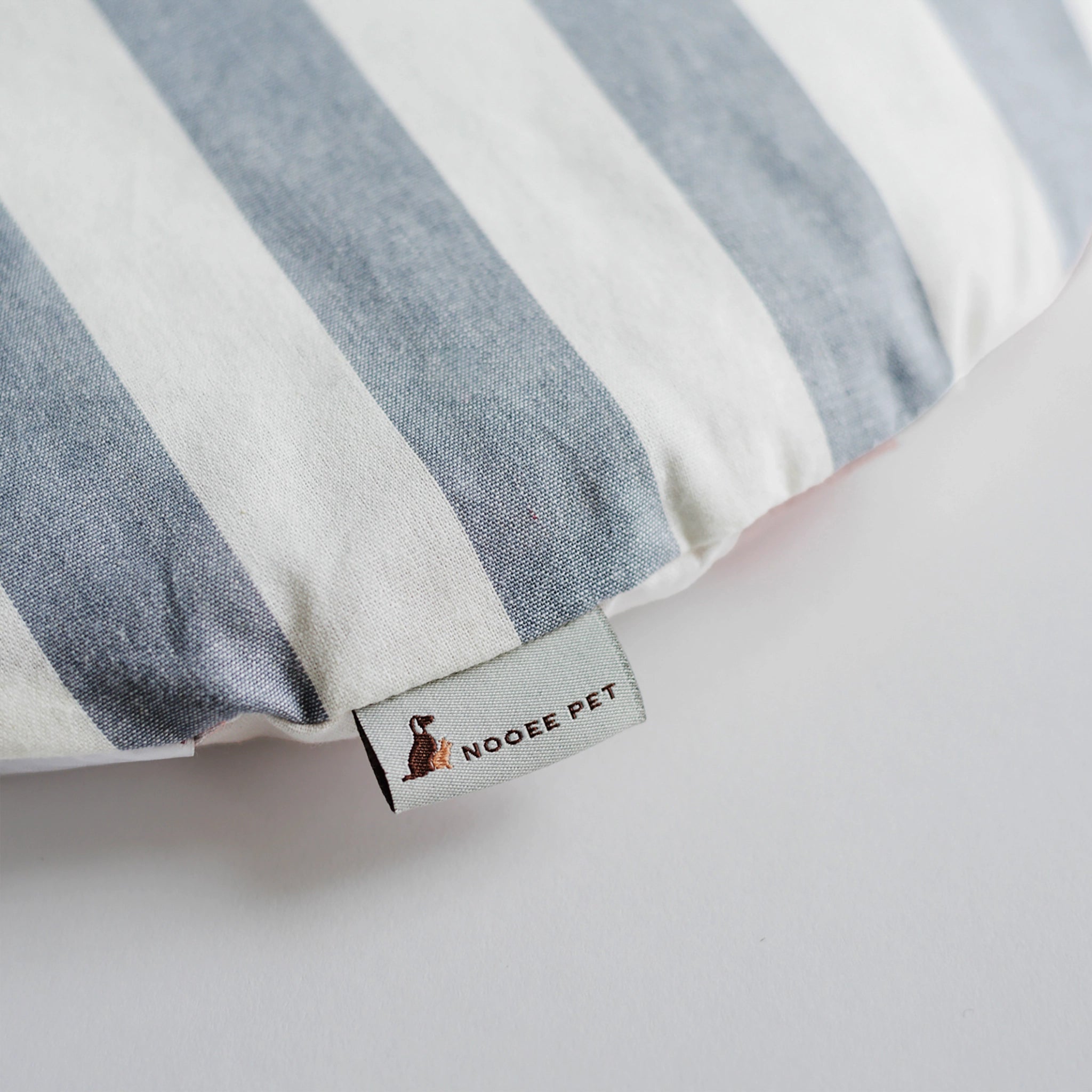 Close-up of the included cushion for the Nooee Pet Harry (XXL) Gray Pet Cave, featuring a stylish blue and white striped fabric with a Nooee Pet logo tag.