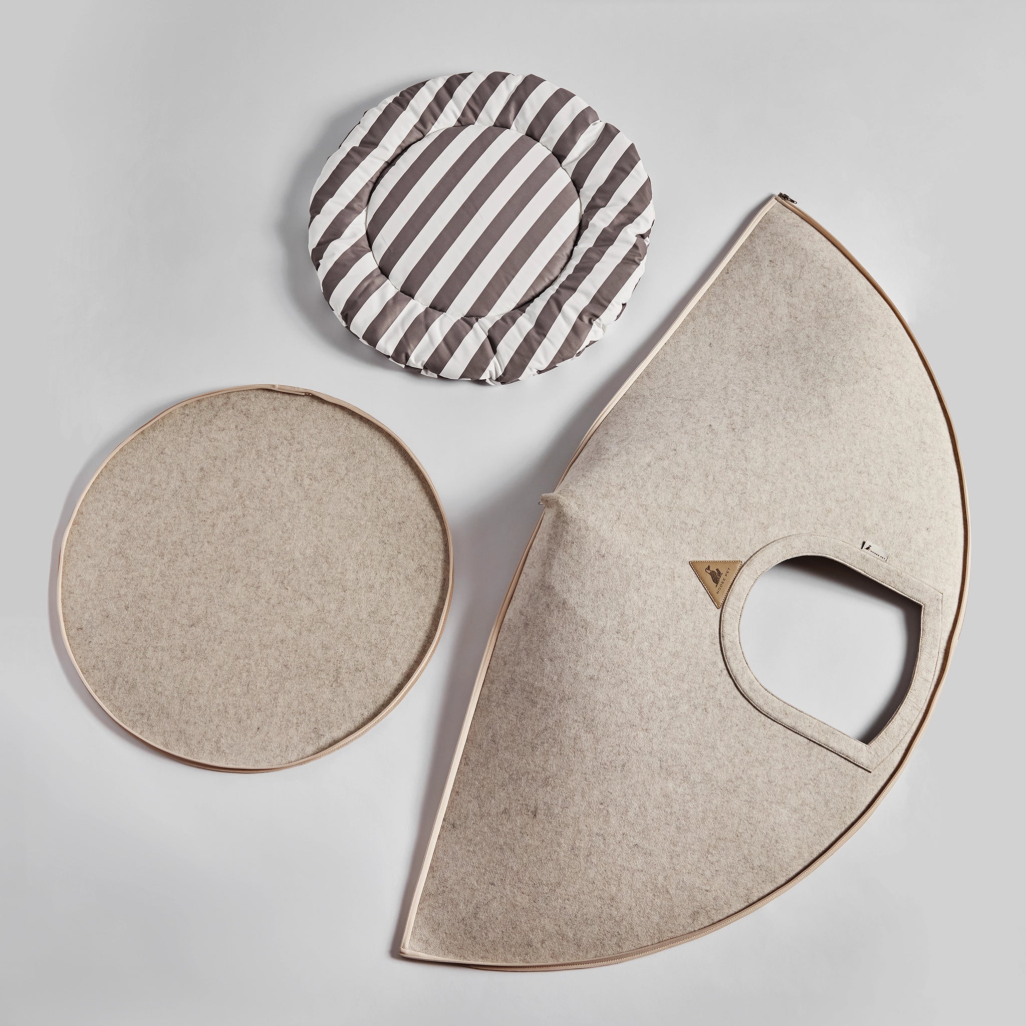 Disassembled Nooee Pet Harry Cave in cream, showing foldable felt panels, a circular base, and a striped cushion.
