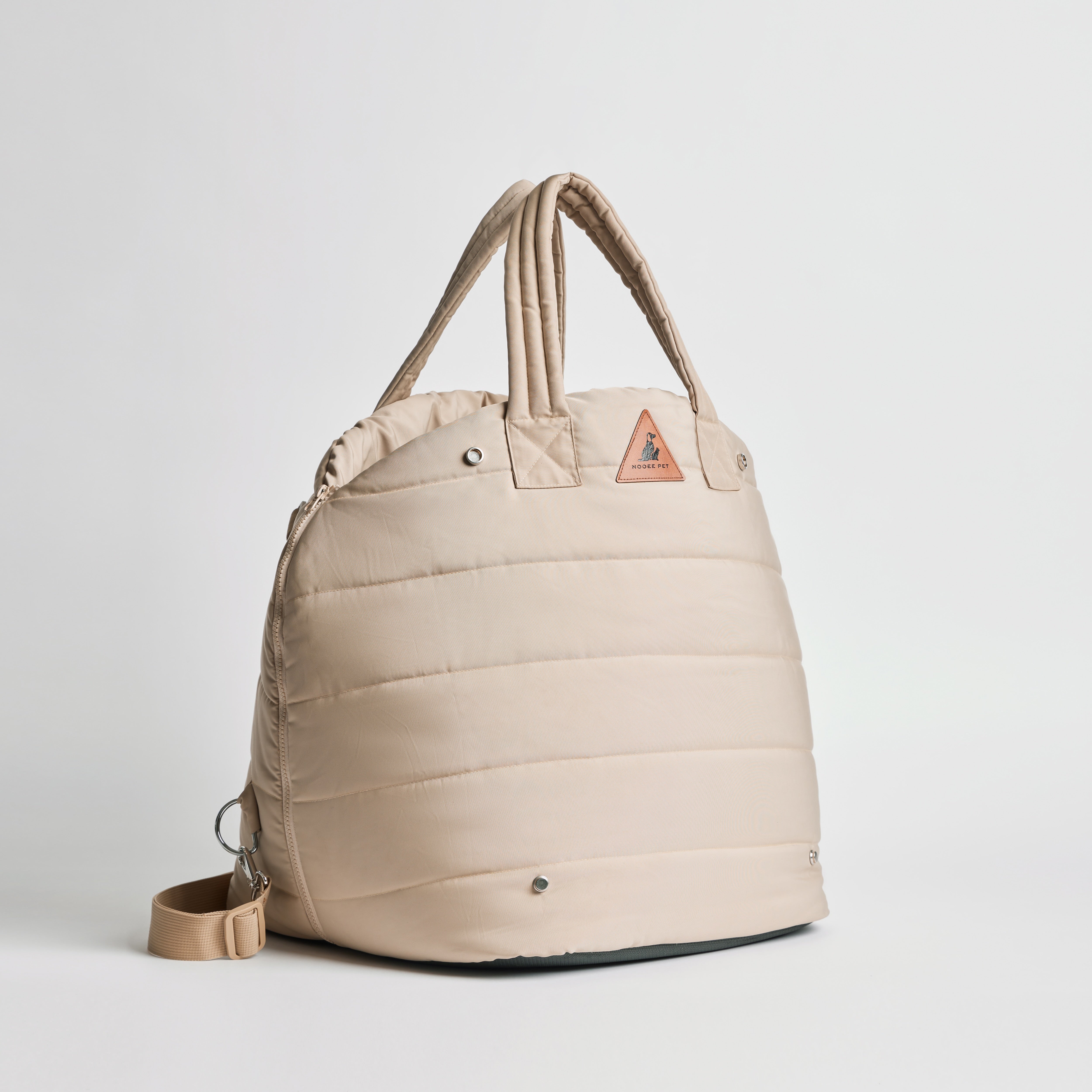 Side view of Nooee Pet Lola Car Seat in cream nylon, featuring padded design, double handles, adjustable shoulder strap, and triangular logo patch on the front.