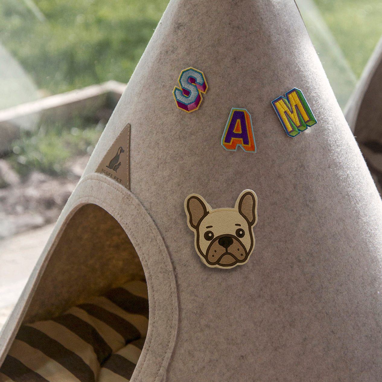 Nooee Pet felt teepee decorated with colorful letter patches spelling “SAM” and a French Bulldog face patch, placed near a window with natural light.
