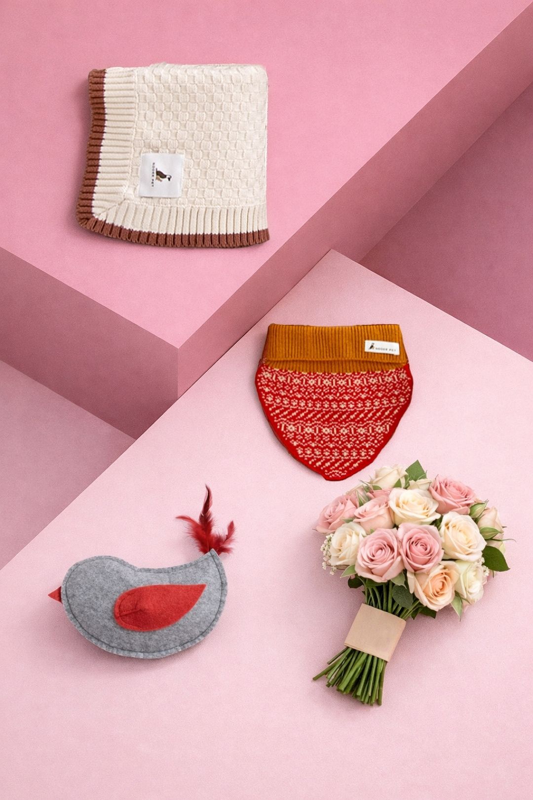 Colorful pet accessories including a knitted dog sweater, pet toy, blanket, and bouquet arranged on pastel geometric surfaces.