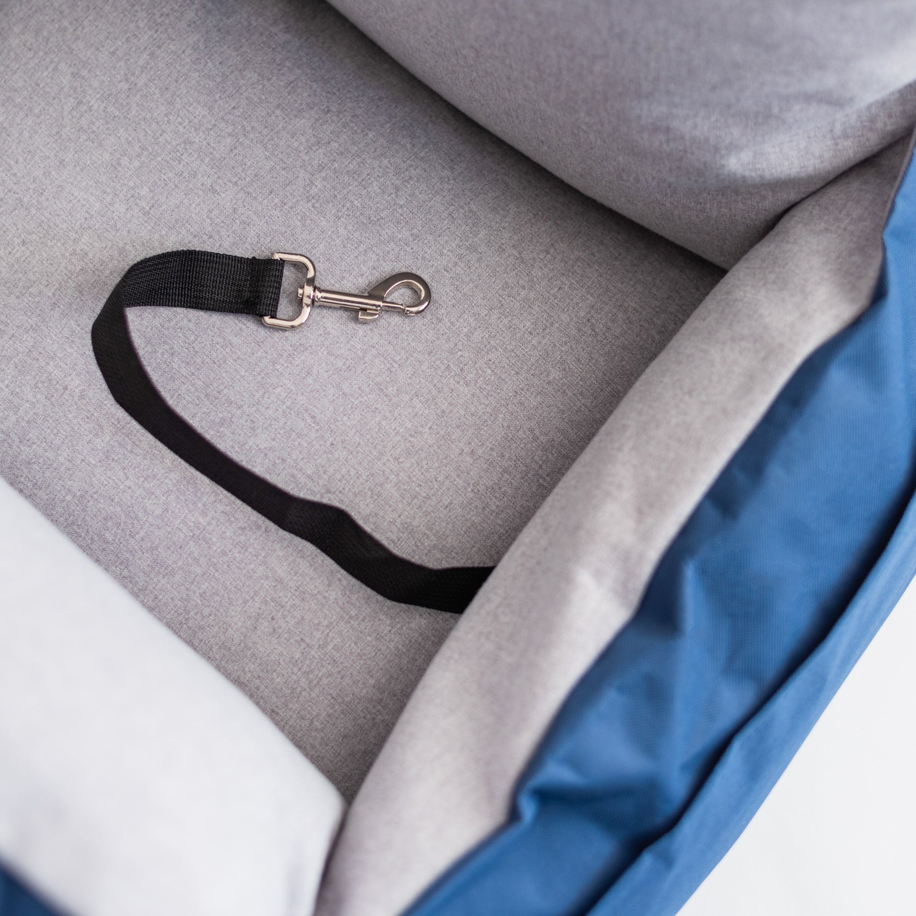 Close-up of the Nooee Pet Car Seat Charlie's inner safety tether, featuring a black strap and metal clip attached to the soft gray cushioned interior.