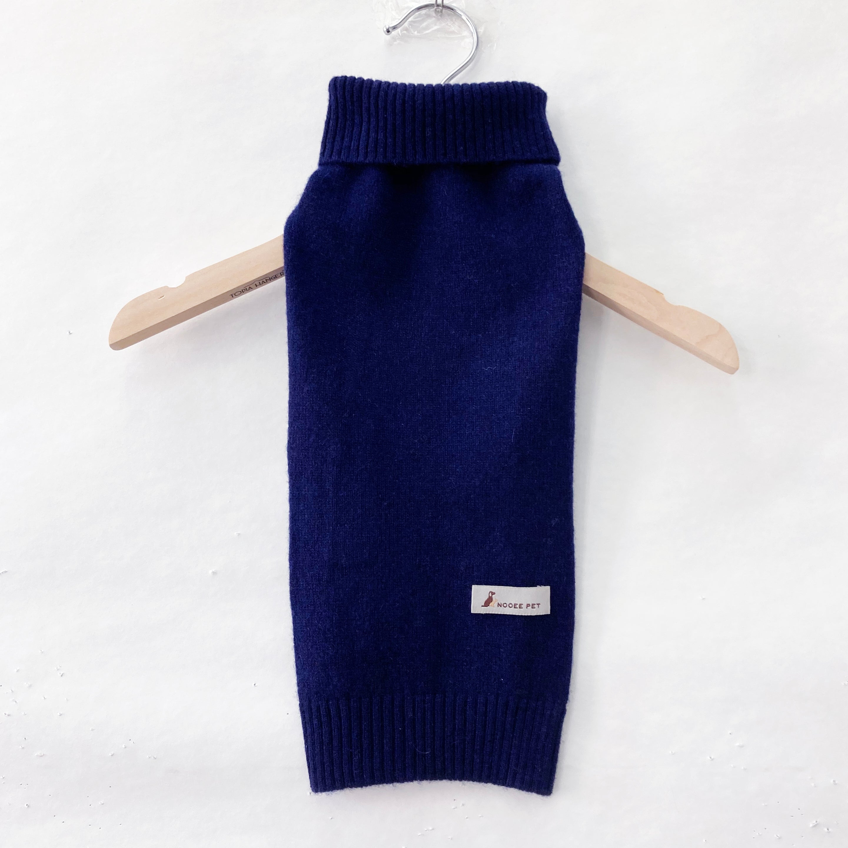 Front view of the Nooee Pet navy blue cashmere dog sweater on a wooden hanger, featuring a ribbed turtleneck and Nooee Pet logo tag near the hem.