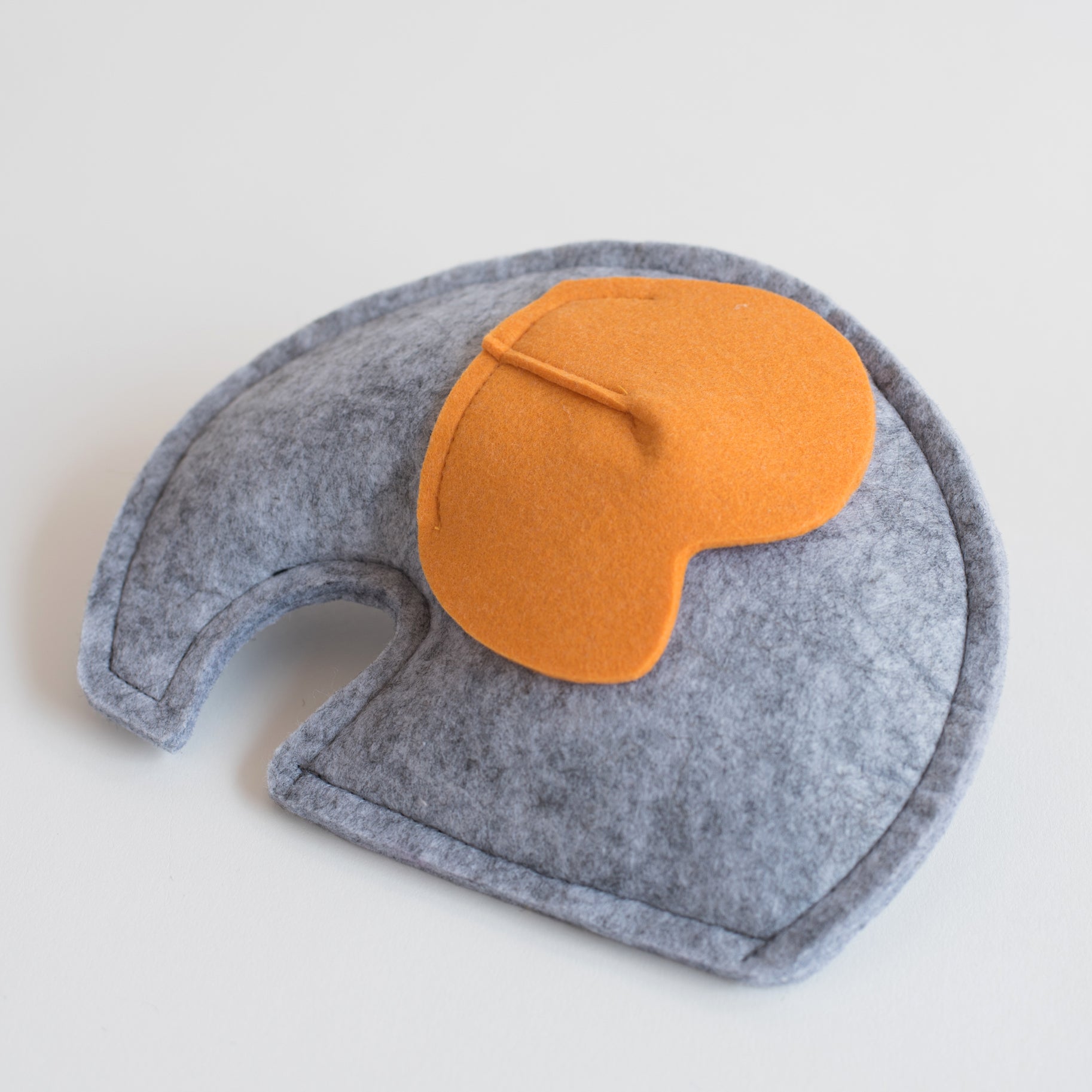 Gray felt elephant-shaped toy with a contrasting orange ear, displayed on a white background.