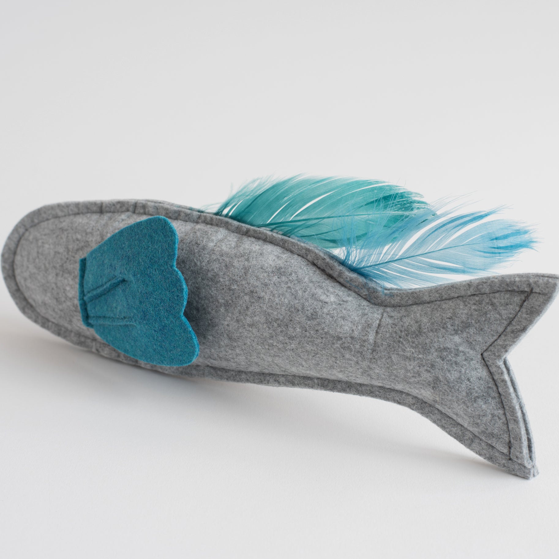 Gray felt fish-shaped toy with a blue felt fin and matching feather tail, displayed on a white background.