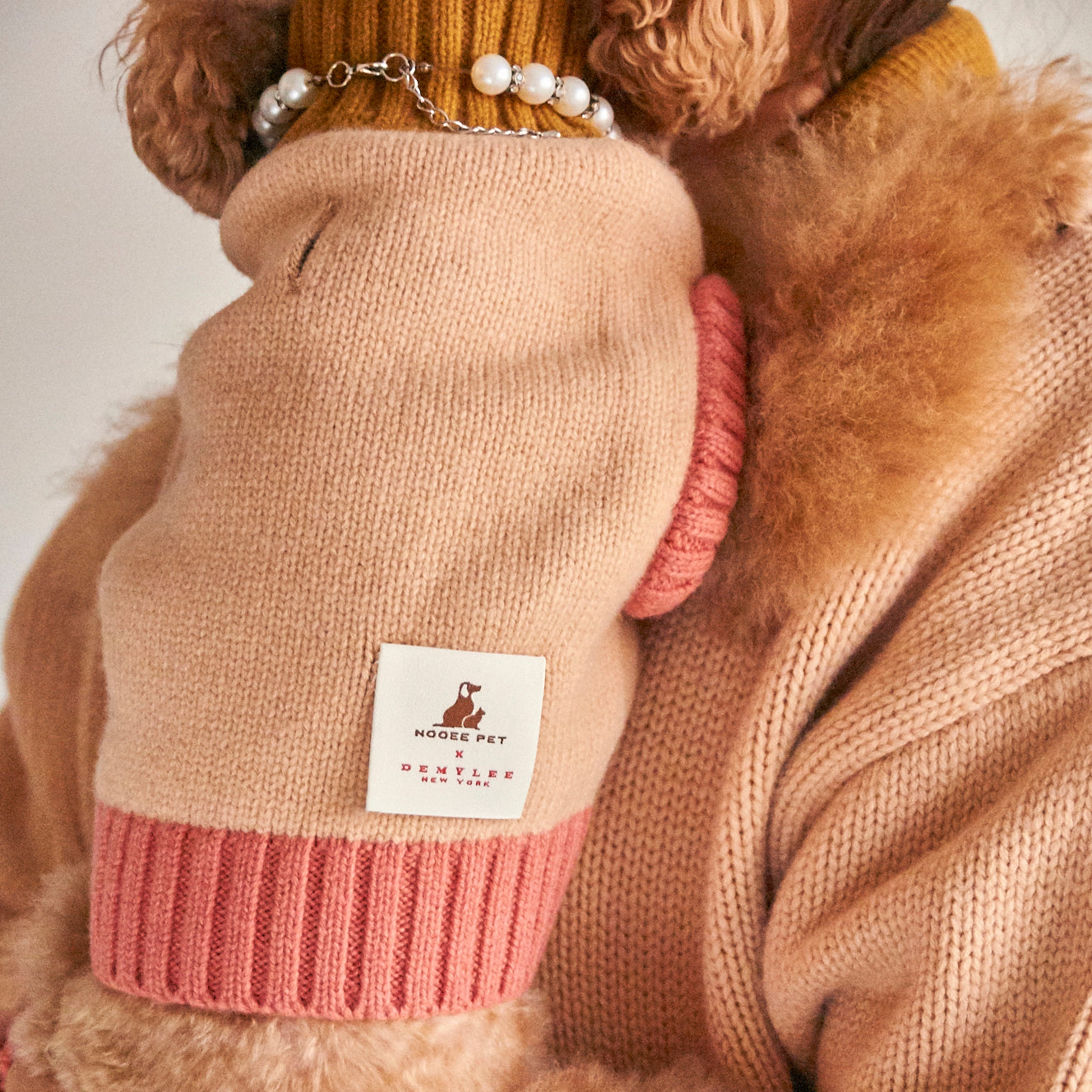 Close-up of Nooee Pet x DEMYLEE fawn merino wool dog sweater featuring a white logo tag, pink ribbed hem, and armhole detail.