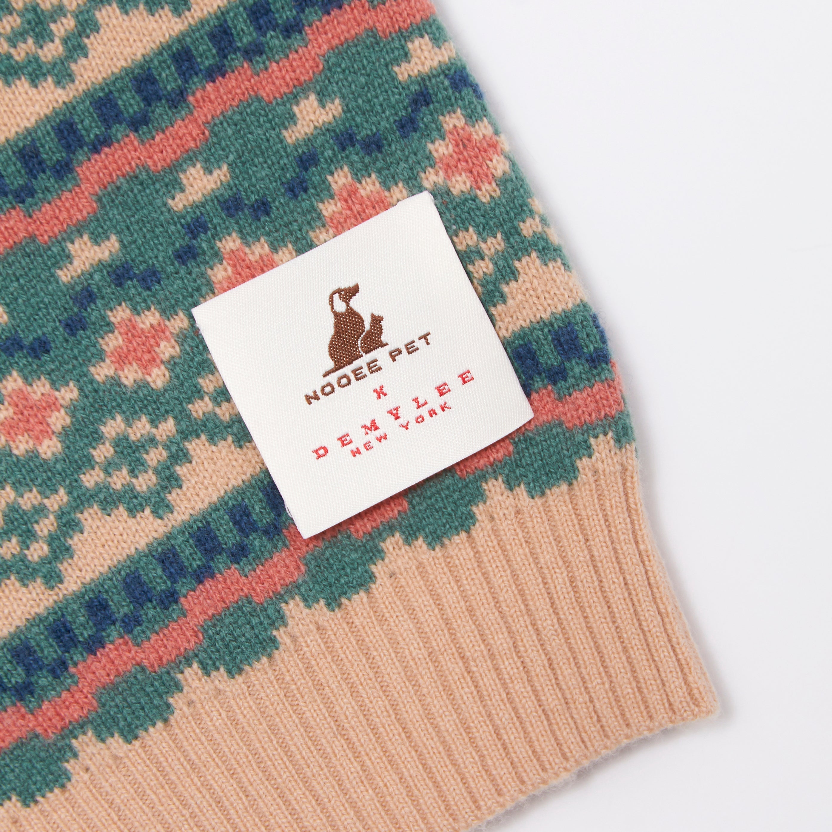 Close-up of the Nooee Pet x DEMYLEE Jacquard Wool Sweater label, showcasing the collaboration tag on a colorful fair isle knit pattern with ribbed trim.