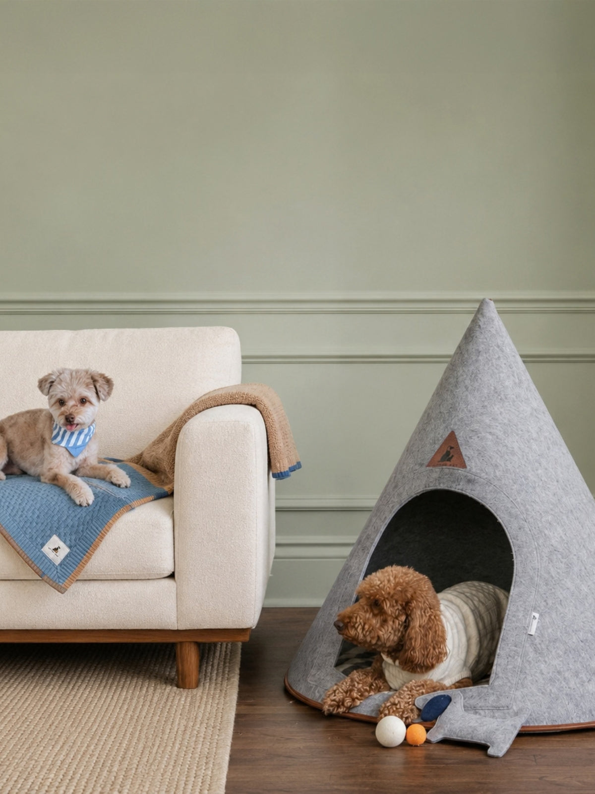 Gray felt Pet Cave with a dog inside beside a cream sofa with another dog on a blue blanket in a modern living room.