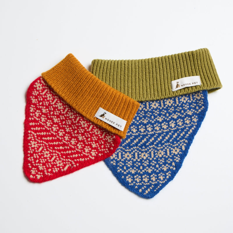 Two Nooee Pet wool dog neck warmers laid flat on a white background—one in red with an amber collar, and the other in blue with a green collar, both featuring intricate knitted patterns and Nooee Pet labels.