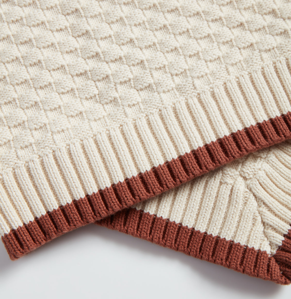Close-up of Nooee Pet Organic Cotton Blanket showcasing the textured knit pattern and ribbed brown trim on cream-colored fabric.