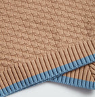 Close-up of brown Nooee Pet organic cotton blanket featuring a waffle-knit pattern and light blue ribbed trim.