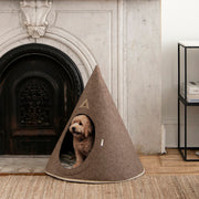 Brown Nooee Pet felt cave with a small dog sitting inside beside a fireplace