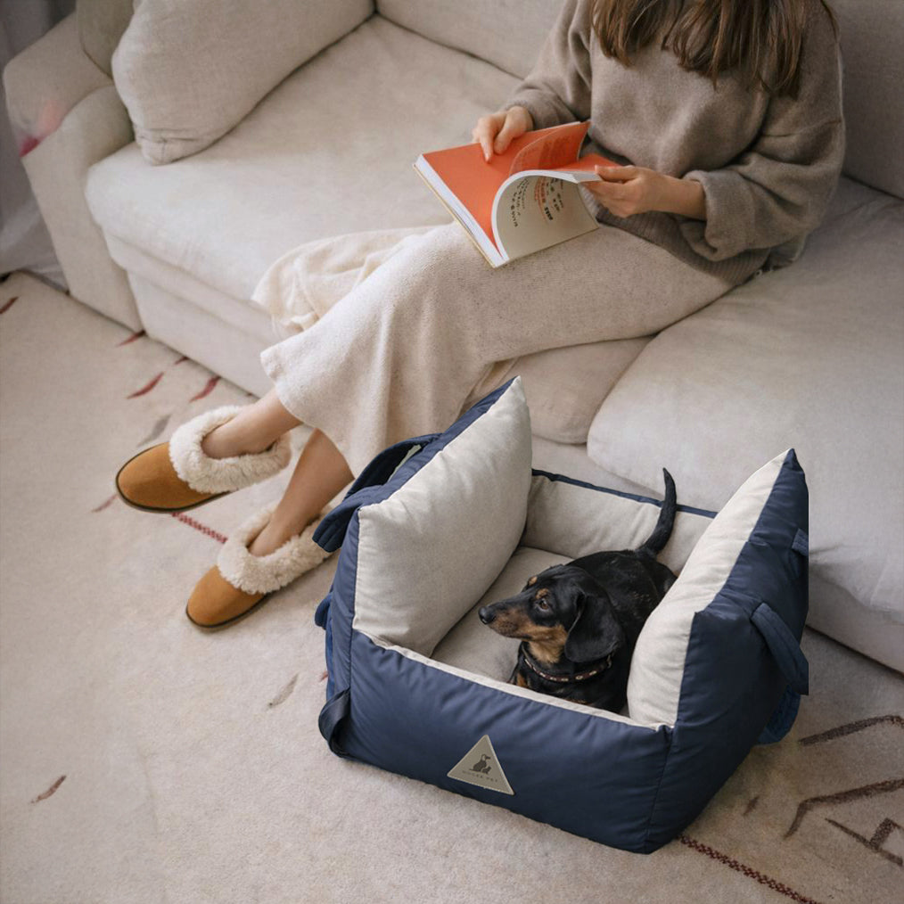 Small dog resting in a navy Nooee Pet car seat beside a sofa