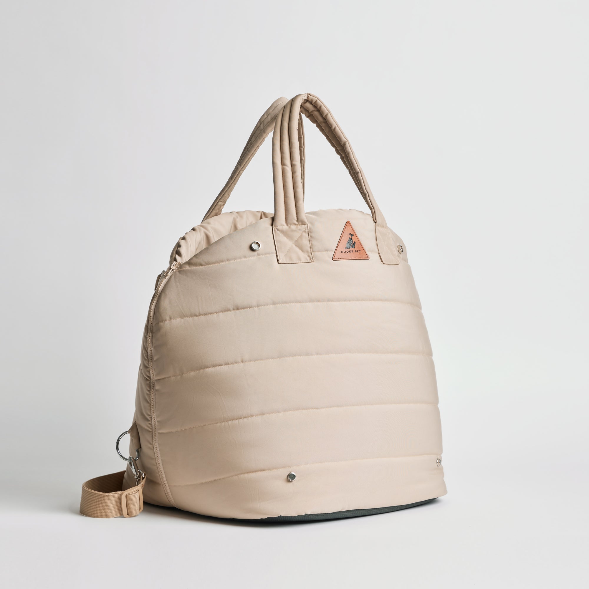 Side view of Nooee Pet Lola Car Seat in cream nylon, featuring padded design, double handles, adjustable shoulder strap, and triangular logo patch on the front.