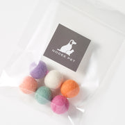 Top view of six multicolored handmade wool pet toy balls, Pastel Set, in a branded Nooee Pet pouch.
