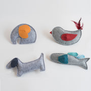 Four felt animal-shaped pet toys in various colors and designs, including a gray dog, elephant, fish with feathers, and bird with red wing and feathers, arranged on a white background.
