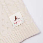Close-up of the Nooee Pet x DEMYLEE New York collaboration label stitched onto the off white wool cable dog sweater.